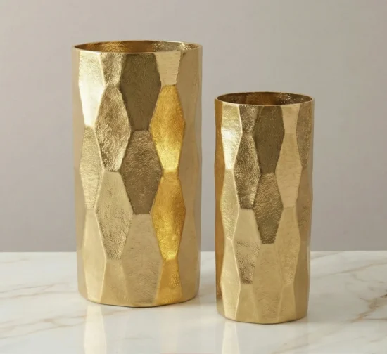 Set of two gold cylindrical metal vases with faceted honeycomb texture.